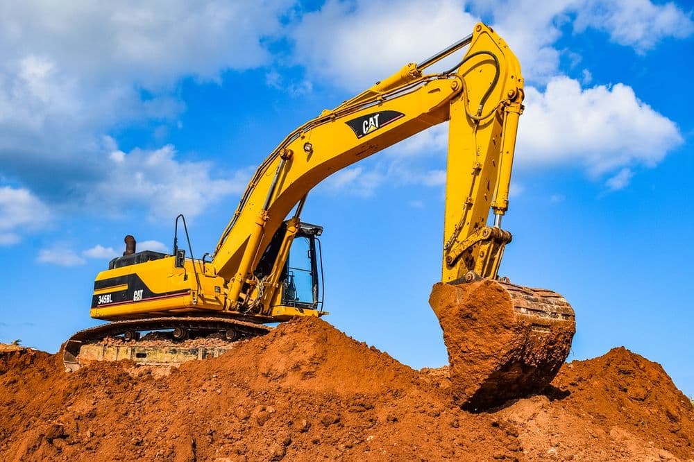 Yellow CAT excavator digging into a mound of red dirt under a blue sky.