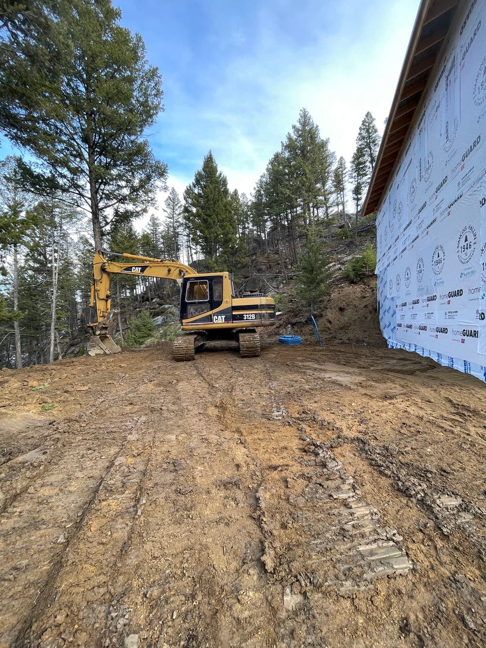 Caterpillar excavator on a construction site surrounded by trees and building materials.