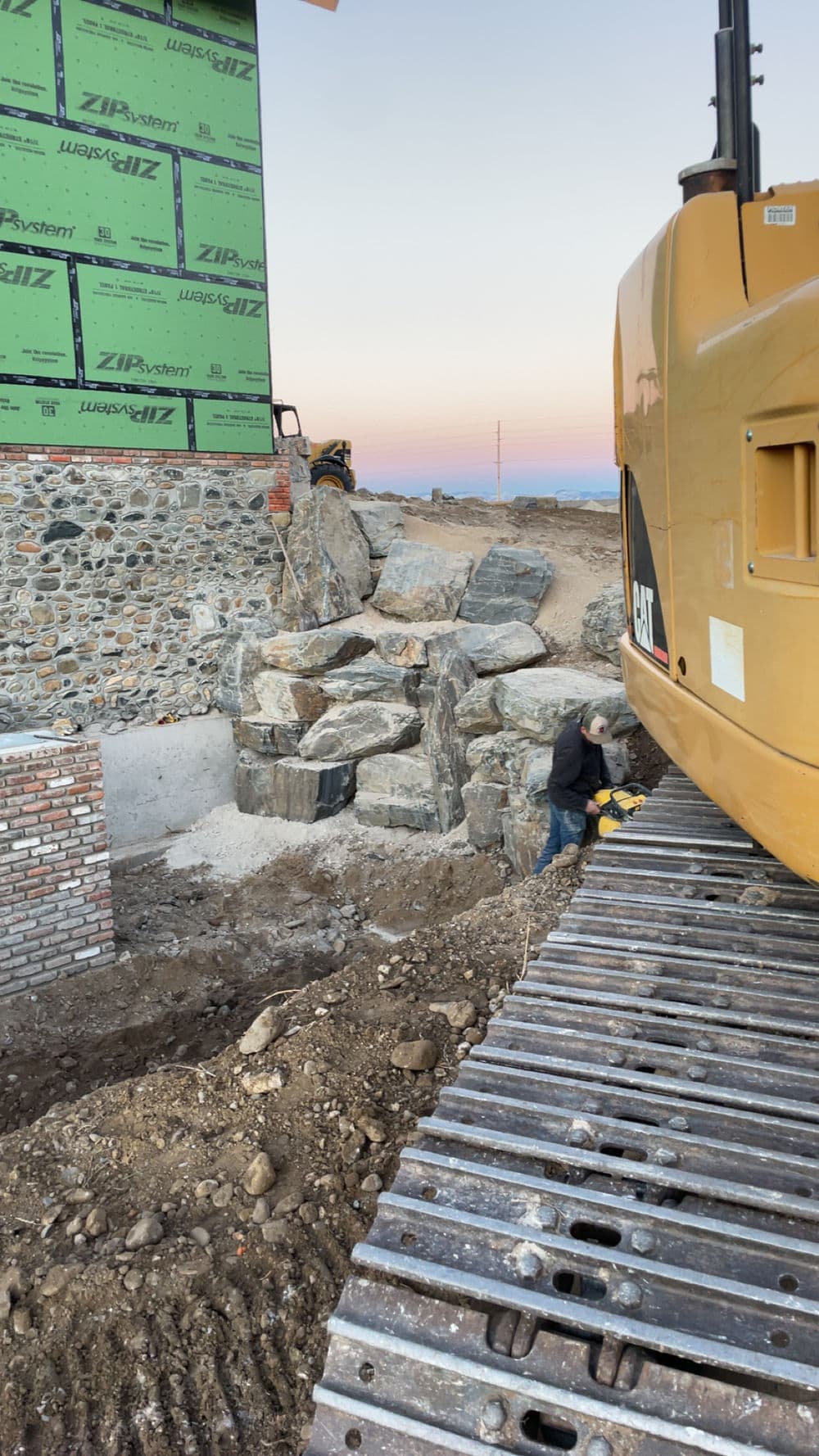 Construction site with heavy machinery and stone structures under a gradient sky.
