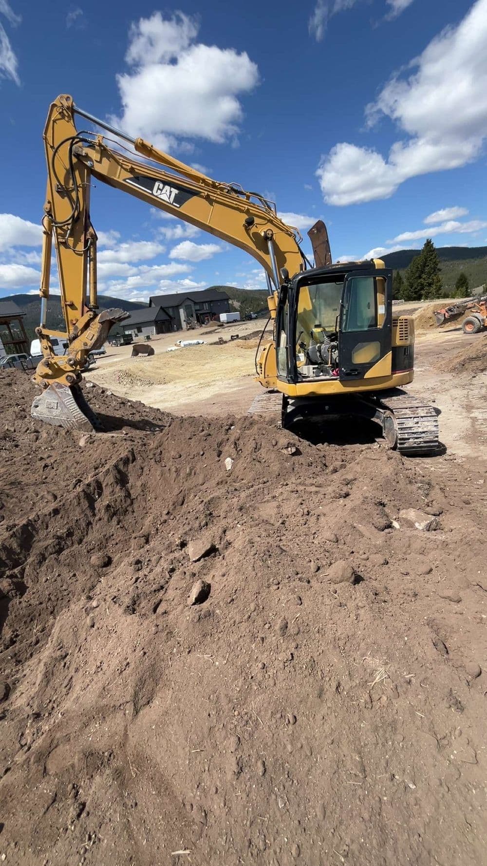 Excavator on construction site digging into dirt under a clear blue sky.