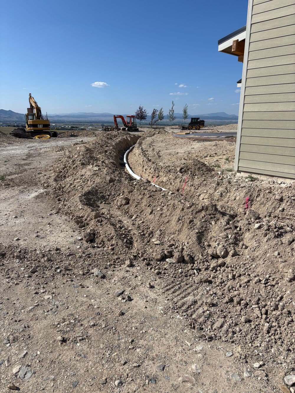 Excavated trench for utility installation near construction site with machinery in the background.