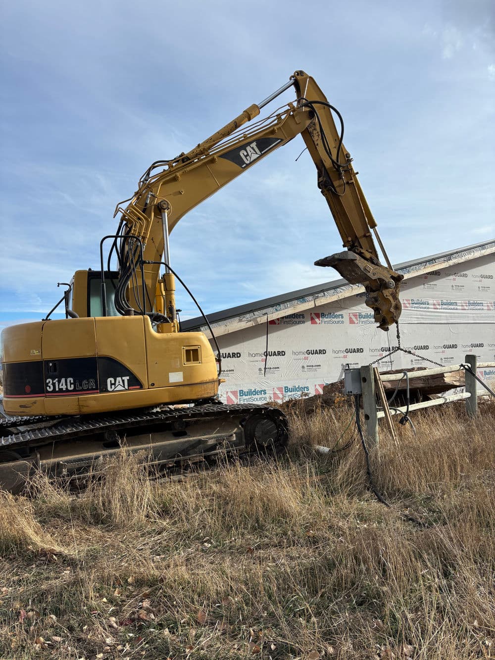 Yellow CAT 314C LCR excavator beside a building site with protective wrap.